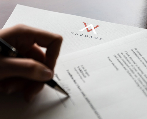 Close up of a woman signing a Vardags letter, on a dark wooden desk