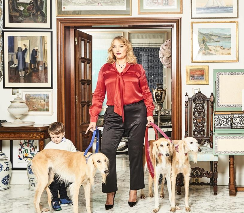 Ayesha Vardags dressed in red, alongside her son and three dogs, all stood in a grand gallery room